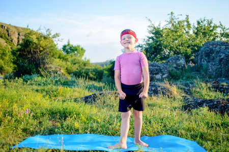 Young Boy Wearing Fitness Attire, Standing on Blue Mat at the Green Grasses and Smiling at the Camera.の写真素材