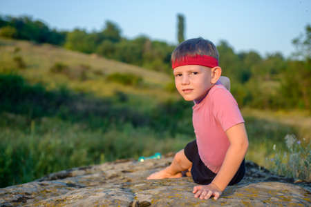 Athletic Handsome Boy Looking at the Camera While Doing Side Planking Exercise on Top of Boulder at the Fieldの写真素材