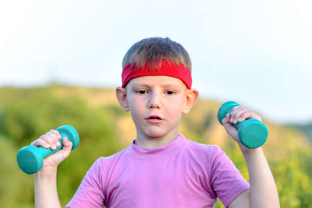 Close up Fit Young Handsome Boy with Red Headband, Lifting Small Weights While Looking Into the Distance in Thoughtful Facial Expression.の写真素材