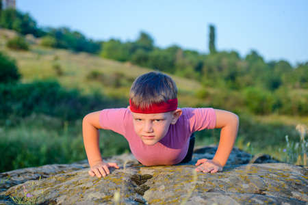 Athletic Young Boy Forcing his Body to Lift While Doing Push Up Exercise on Top of a Big Rock with Sacrificing Facial Expression.の写真素材