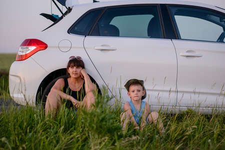 Serious Mom with is Cute Son Sitting Beside their White Car While Waiting for Something.の写真素材
