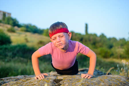 Athletic Young Boy Forcing his Body to Lift While Doing Push Up Exercise on Top of a Big Rock with Sacrificing Facial Expression.の写真素材