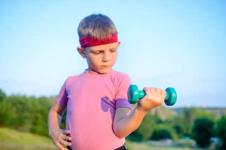 Close up Strong Cute Boy with Red Headband Doing an Outdoor Exercise and Lifting Small Dumbbell...