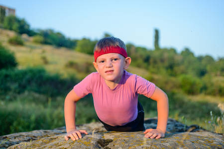 Athletic Young Boy Forcing his Body to Lift While Doing Push Up Exercise on Top of a Big Rock with Sacrificing Facial Expression.の写真素材