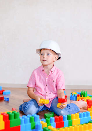 Creative young boy wearing a hardhat sitting on a hardwood floor thinking about what to build with his colorful plastic building blocksの写真素材