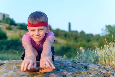 Little boy working out on a rock outdoors doing stretching exercises reaching forwards to touch his toesの写真素材