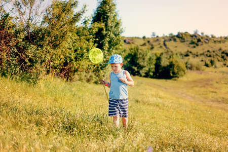 Little boy catching insects with a net in a rural meadows as he enjoys the freedom of his summer vacationの写真素材