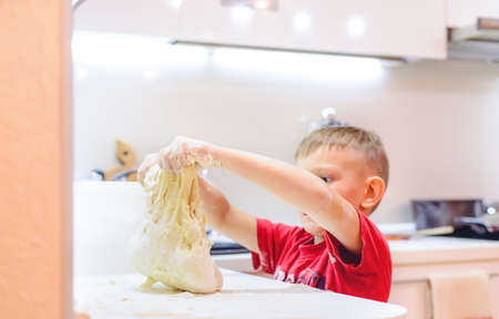 Young boy playing with dough while baking covering his arms in the uncooked mixture with a funny expression on his face as he stands at the kitchen counterの写真素材