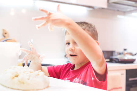 Little boy having fun playing with dough in the kitchen standing at the counter kneading it with his fingers, close up viewの写真素材