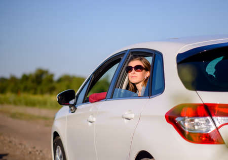 Smiling young lady wearing trendy sunglasses riding in the rear passenger seat in a car looking out...
