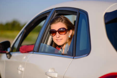 Friendly smiling young woman in a car looking out of the rear passenger window in a pair of trendy...