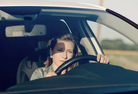 Female driver checking her side mirror as she pulls away into the street after being parked alongside a rural roadの写真素材