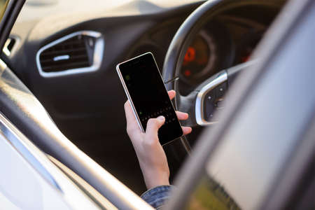 View from behind through the open window of a girl reading a text message as she drives along in her car with the blank screen visible to the viewerの写真素材