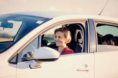 Smiling blond woman driving a car on a sunny summer day viewed through her open side windowの写真素材