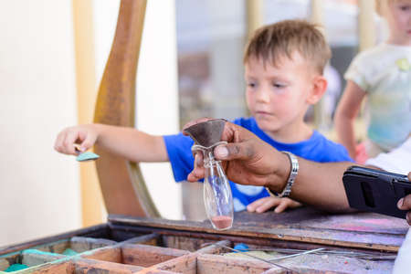 Small boy filling a glass bottle with colorful pigments in powder or sand as he creates his own imaginative multicolored artworkの写真素材
