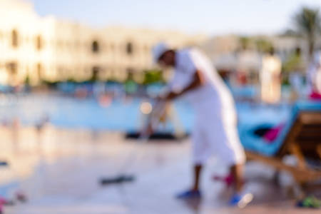 Blurred background of a tourist at a summer holiday resort in the tropics standing bending forward in front of a large swimming pool and the apartments or hotelの写真素材