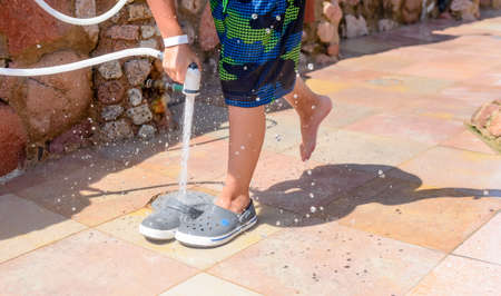 Young boy rinsing beach sand off his legs and shoes with a hose pipe at a seaside resort on his summer vacationの写真素材
