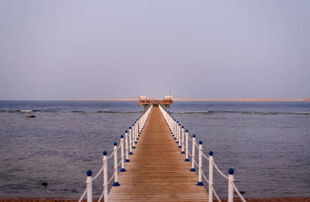 Wooden jetty off a tropical beach leading away from the camera over te tidal zone to beach huts on the end overlooking a calm oceanの写真素材