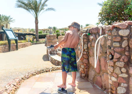 Little boy hosing off his shoes and feet with a jet of fresh water at a seaside resort after spending the day on the beach to wash off the sand and saltの写真素材