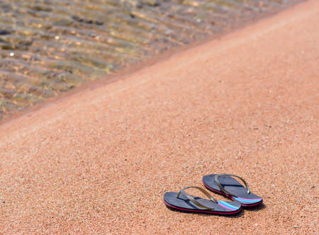 Pair of Flip Flop Thongs Resting Along Shoreline of Sandy Beach with Clear Water