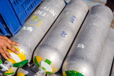 Row of full oxygen tanks for scuba diving at a resort or club with a mans hand visible touching one on the leftの写真素材