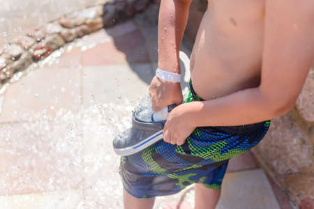 Little boy hosing off his shoes and feet with a jet of fresh water at a seaside resort after spending the day on the beach to wash off the sand and saltの写真素材
