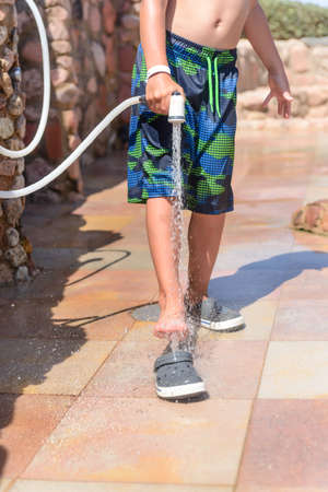Young boy rinsing off his feet and shoes to get rid of the salt and sand after spending the day at the beach at a seaside resort on summer vacationの写真素材