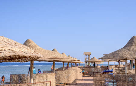Thatched beach umbrellas and recliner chairs on a beach at an idyllic tropical resort for a summer...