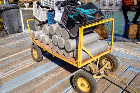 Trolley loaded with scuba diving equipment piled with flippers and oxygen and air tanks ready to be taken out for a deep sea dive at a tropical resort on summer vacationの写真素材