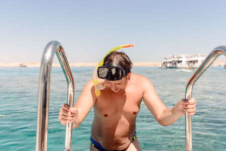 Smiling man preparing to go snorkeling standing holding onto the rails on a dive boat with the ocean behindの写真素材