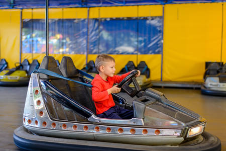 Smiling young boy sitting behind the wheel in a bumper car at an amusement park or fairground as he steers himself around the trackの写真素材