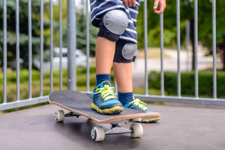 Close up of the legs of a young boy with his skateboard on a ramp dressed in colorful trainers and protective knee capsの写真素材