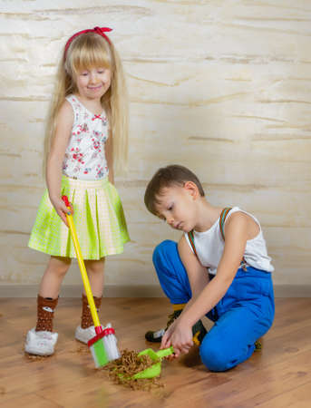Young boy and girl helping to clean house using colorful green pans and brushes as they sweep up wood shavings and dirt off a wooden parquet floorの写真素材