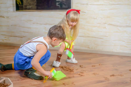 Young boy and girl helping to clean house using colorful green pans and brushes as they sweep up wood shavings and dirt off a wooden parquet floorの写真素材
