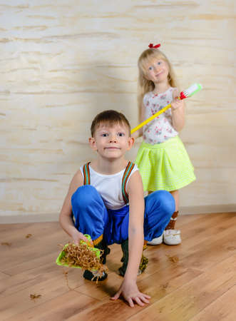 Young boy and girl helping to clean house using colorful green pans and brushes as they sweep up wood shavings and dirt off a wooden parquet floorの写真素材