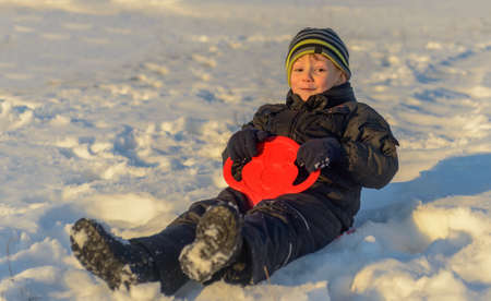 Happy little boy warmly wrapped in winter clothing having fun in fresh white winter snow in evening light as he grins at the cameraの写真素材
