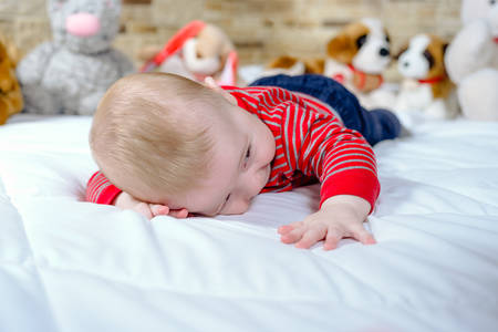 Cute chubby little baby with a happy smile lying on its stomach on a bed with a row of soft cuddly...