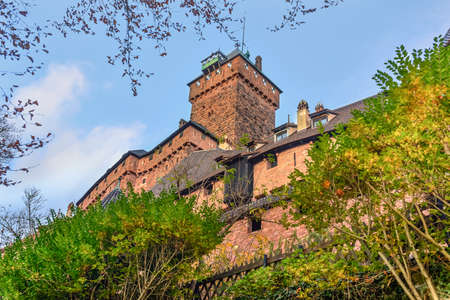 View from below of an old medieval castle of Haut-Koenigsbourg in Alsace or fortress on a hilltop in late autumn or winter with deciduous leafless trees under a cloudy blue skyのeditorial素材
