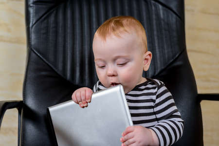 Adorable Baby Boy Holding his Tablet Computer While Sitting on an Office Chair and Looking at the Camera.の写真素材