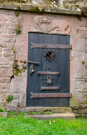 Unique old wooden door with iron plating and log underneath stone engraving of dog overhead in stone boundary wallの写真素材