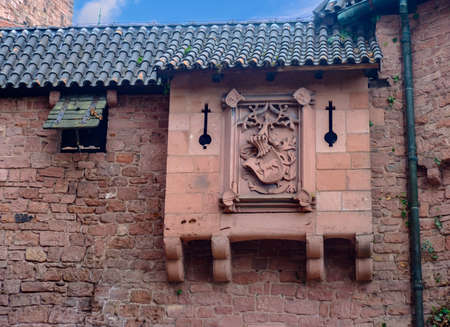 Beautiful red brick castle of Haut-Koenigsbourg in Alsace, France with conical spires and closed windows, surrounded by foliage under blue sky and white cloudsのeditorial素材