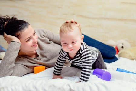 Happy young mother playing with her baby touching him tenderly on the head with a loving smile as they play together on a duvetの写真素材