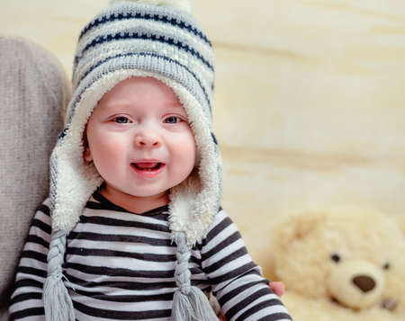 Adorable young baby in a blue and white knitted winter outfit sitting on his mothers lap as she dresses him with matching blue shoes or bootiesの写真素材