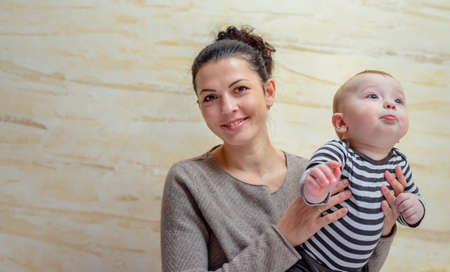 Proud young mother with her baby son held aloft in her arms grinning joyfully at the camera, with...
