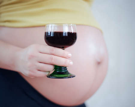 Selective focus close up view on belly of pregnant woman and hand holding glass full of wineの写真素材