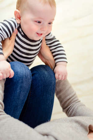 Close up of laughing happy baby in striped shirt being held in hands and on knees of playful parent