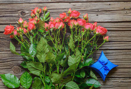 Bouquet of lovely freshly cut pink roses on stems by small blue present tied with ribbon against a wood backgroundの写真素材