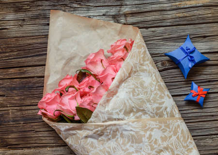 Wrapped bouquet of pink roses with Valentines gifts for a sweetheart in decorative blue boxes on a rustic wooden table, overhead viewの写真素材