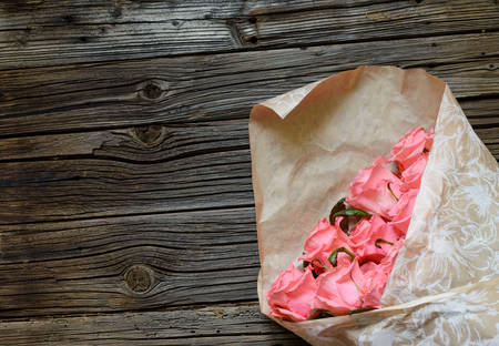 Bouquet of gift wrapped pink roses symbolic of love, romance, Valentines Day, Mothers Day or anniversary on a rustic wood background with copy spaceの写真素材