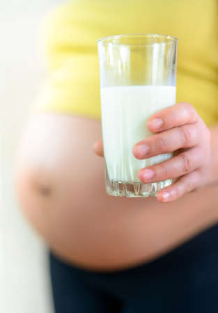 Pregnant woman holding a healthy glass of farm fresh milk rich in calcium, close up of her bare belly and handの写真素材